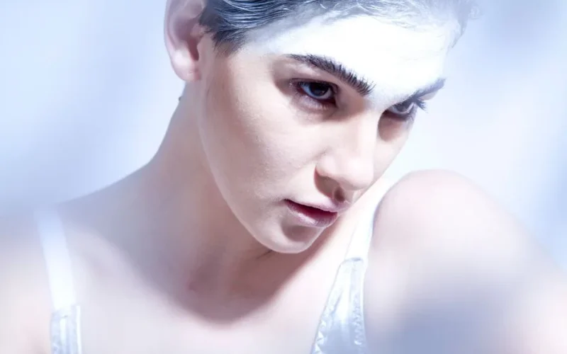 Close-up artistic portrait of a woman with white makeup, conveying emotion and intensity.
