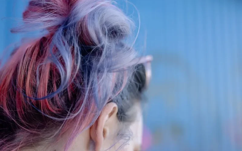 Close-up view of vibrant pink and purple dyed hair against a blue background.