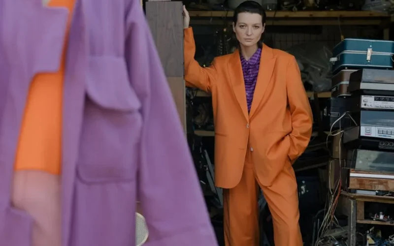 Fashionable woman poses in a vibrant orange suit indoors. Modern style and bold colors.