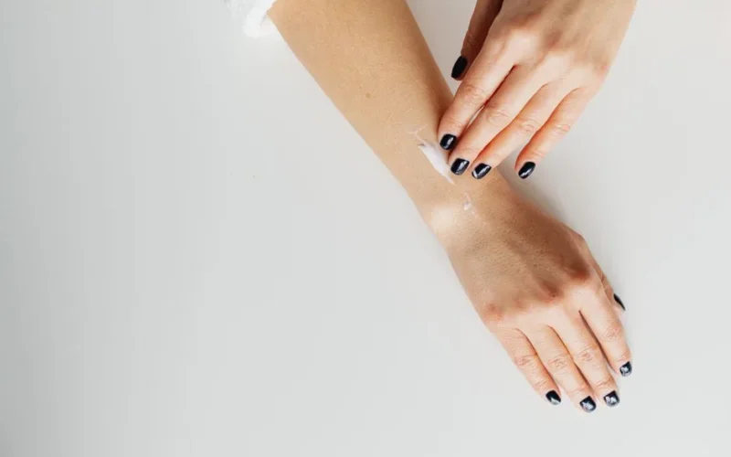 A close-up view of hands applying moisturizing cream on skin on a white background.