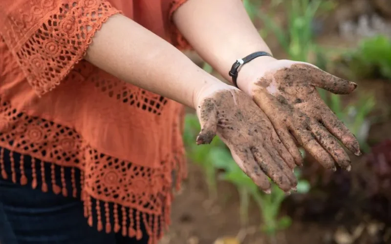 A woman shows her muddy hands while gardening outdoors, symbolizing connection with nature.
