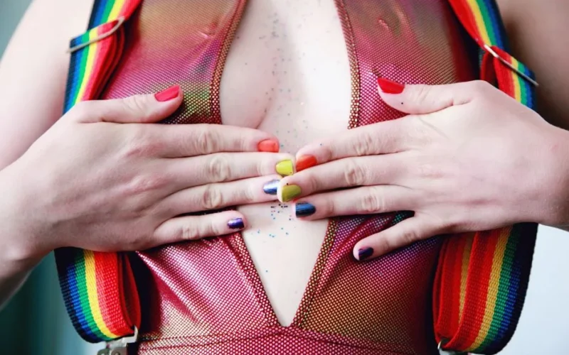 Close-up of a woman's hands with rainbow nails and suspenders, showcasing vibrant style.