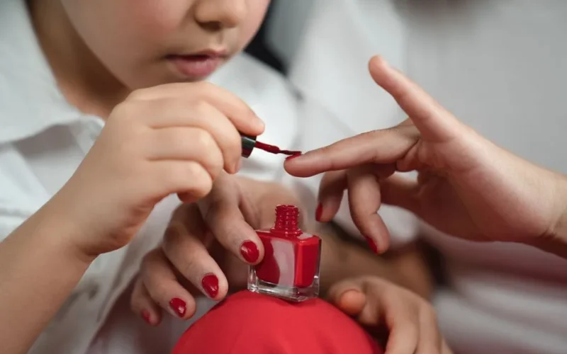 A close-up of a child painting their mother's fingernails red, showcasing a bonding moment.