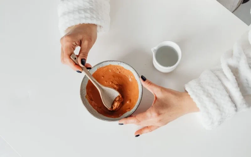 Woman in bathrobe mixing homemade clay mask in a bowl, ideal for skincare DIY concepts.
