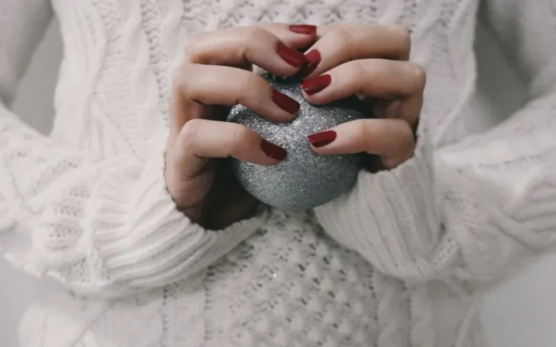 Hands with red manicure holding a silver glitter ball, perfect for winter holiday themes.