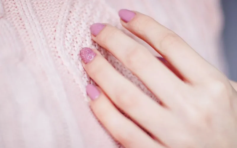 Close-up of a woman's hand with pink manicure resting on a soft knit sweater, showcasing elegance and fashion.