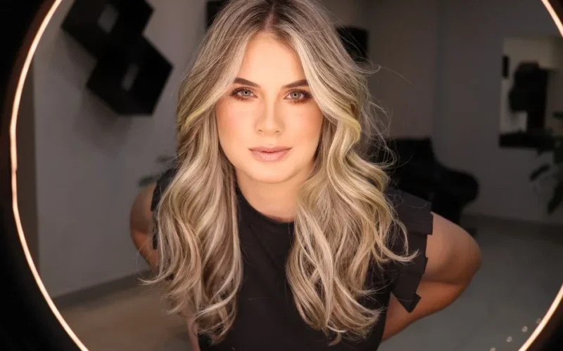 Close-up portrait of a blonde woman with stylish makeup and elegant curls, looking confidently into the camera.