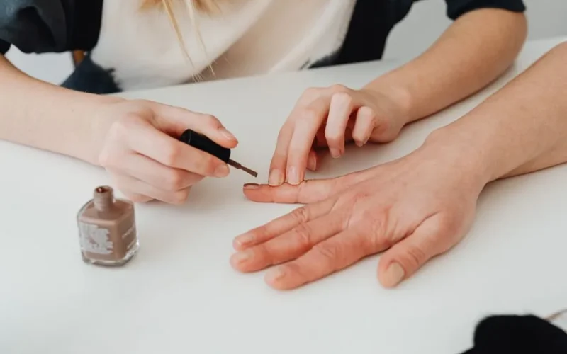 Close-up of hands during a manicure session, applying nail polish in a salon setting.