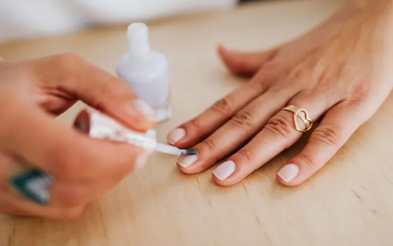 Detailed view of a hand receiving a manicure with nail polish application and a gold heart ring.