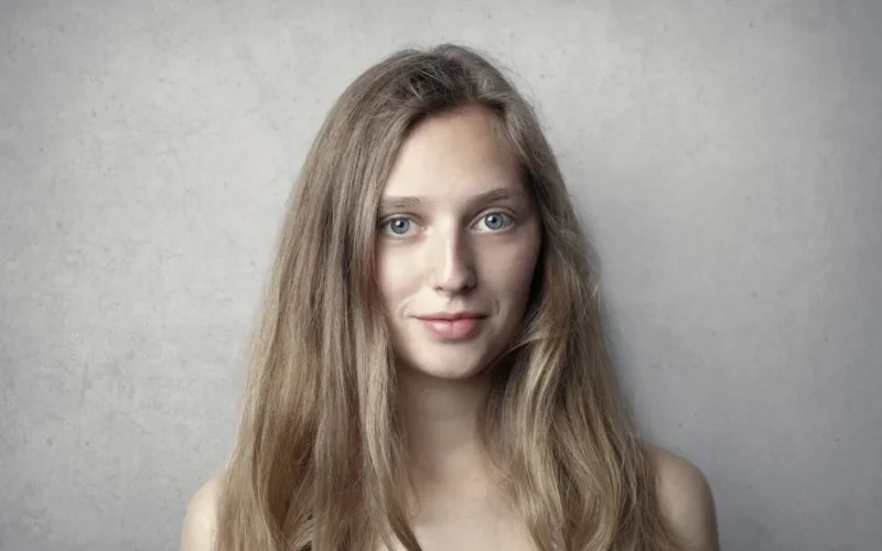 Close-up portrait of a smiling woman with long blonde hair against a gray background.