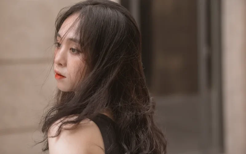 Close-up portrait of a young woman with long tousled hair in an urban setting.