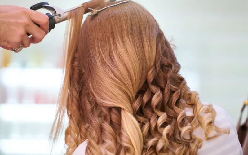 Close-up of a stylist curling blonde hair into glamorous curls at a salon.