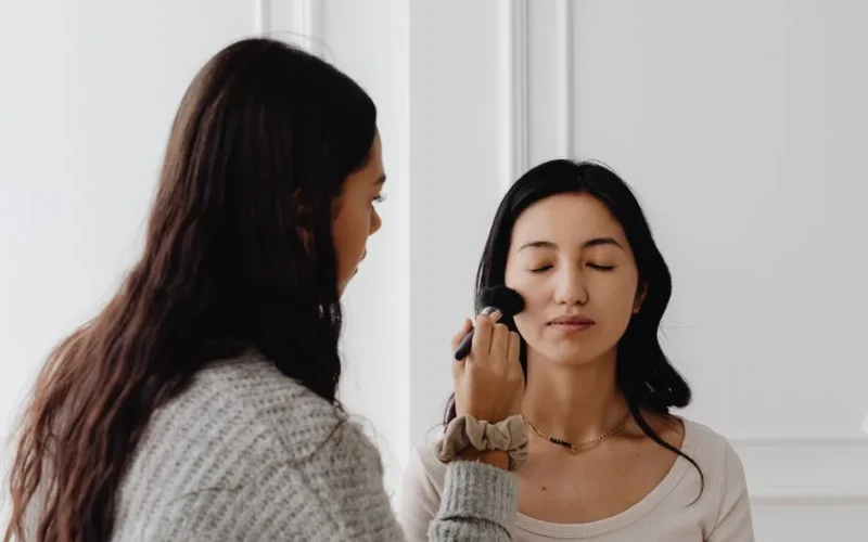 A professional makeup artist applies foundation to a client's face indoors.