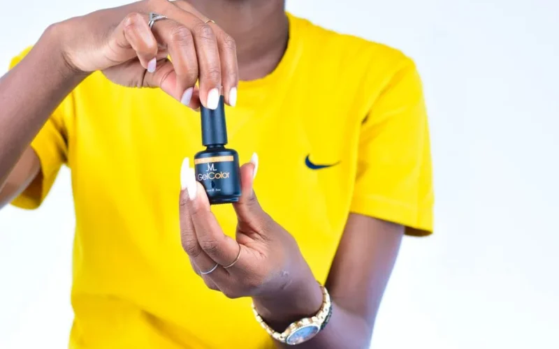 Woman displaying a black GelColor nail polish bottle against a yellow background.