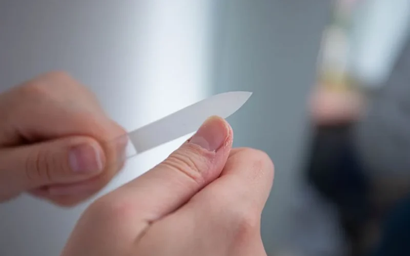 Detailed close-up of a person's hands filing nails with a nail file indoors.