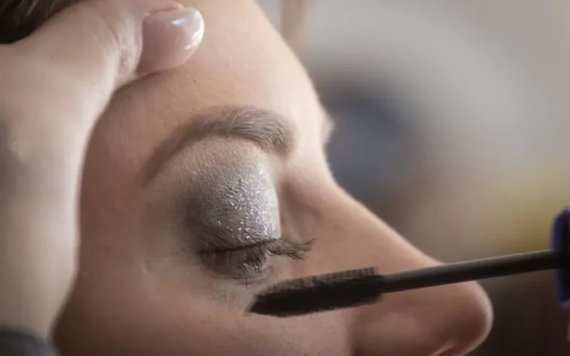 A woman's eyelid is delicately painted with glamorous shimmery eyeshadow and mascara.