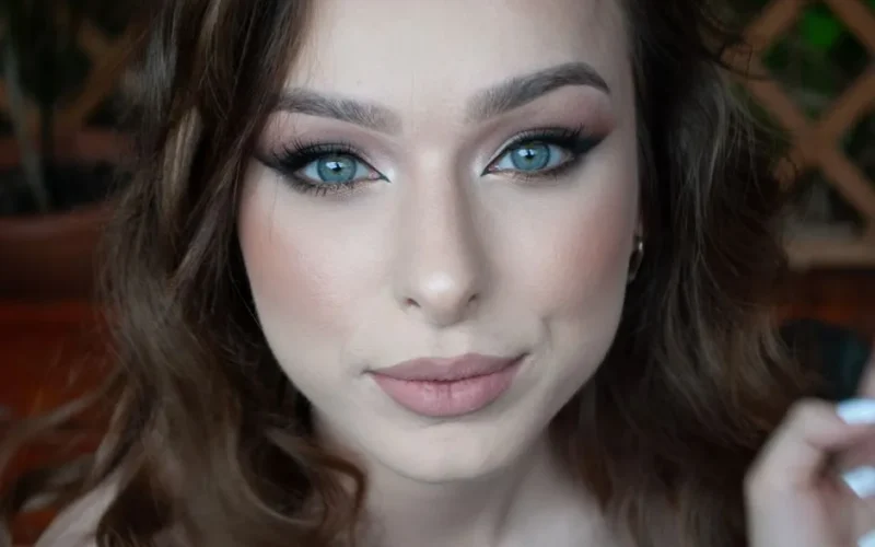 A close-up portrait of a woman with blue eyes and professional makeup, exuding elegance.