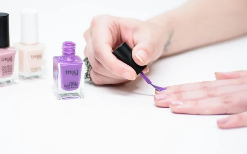 A close-up of a person applying purple nail polish as part of a manicure.