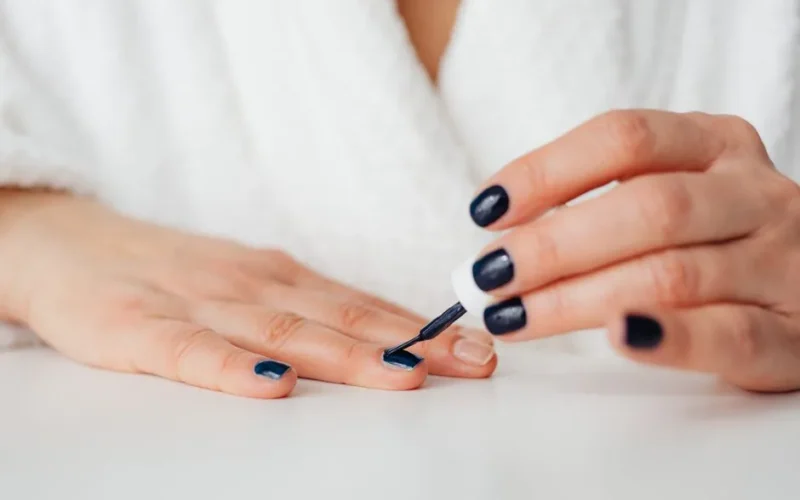 A woman applying dark nail polish at home, showcasing beauty and self-care.
