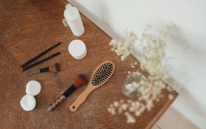Top view of beauty tools and accessories on a wooden table with flowers.