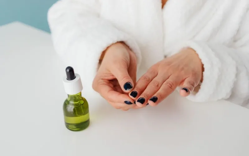 Female in a bathrobe applying serum using a green glass bottle, showcasing self-care routine.