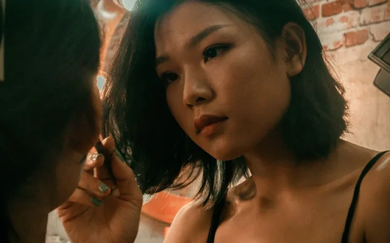 Close-up of a woman applying makeup in an indoor setting with a warm mood.