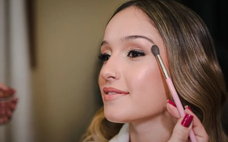 Close-up of a young woman applying makeup with a brush, showcasing beauty and elegance.
