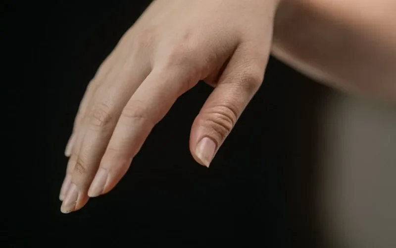 Detailed image of a hand with natural nails, delicately posed against a dark backdrop.