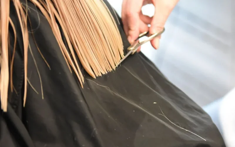 Professional hairdresser cutting blonde hair with scissors in a salon close-up.