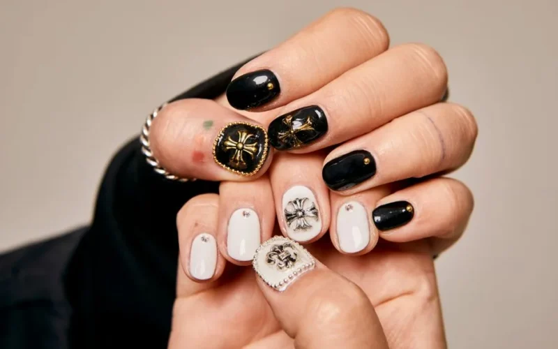 Close-up of women's hands showcasing artistic black and white nail art with ornate embellishments.