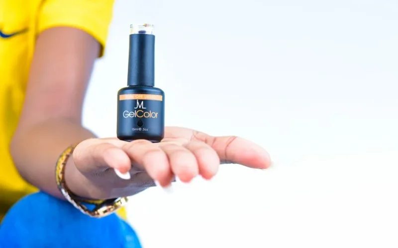 A woman's hand showcasing a gel nail polish bottle against a light background.