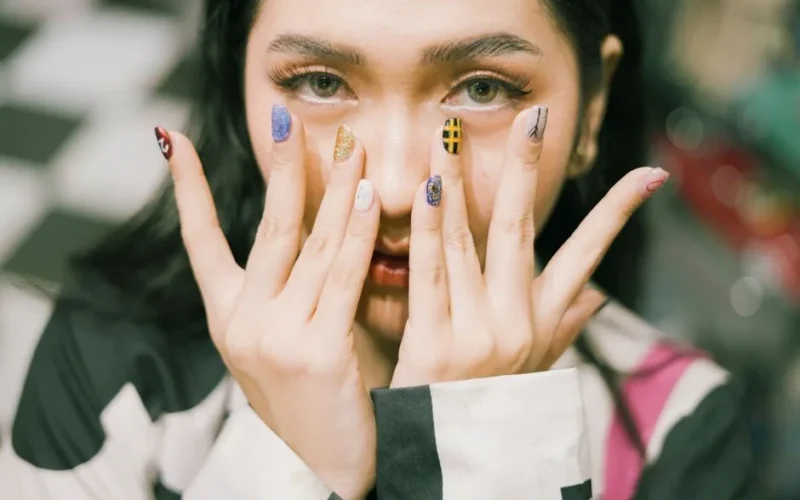 Close-up shot of a woman with colorful acrylic nails covering her face.