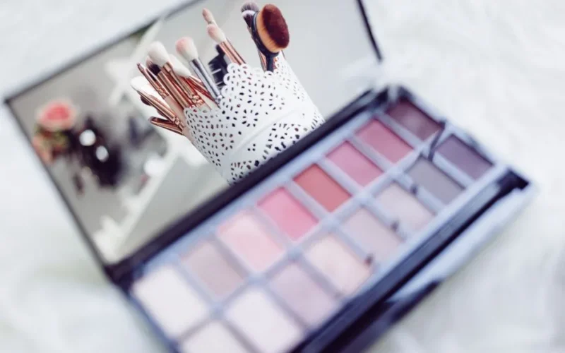 Close-up of makeup brushes in a decorative holder and a colorful eyeshadow palette.