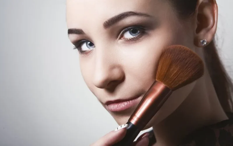 Close-up view of a young woman using a makeup brush, showcasing beauty and cosmetics.