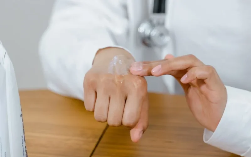 Close-up of a doctor applying lotion on their hand, focusing on skincare.