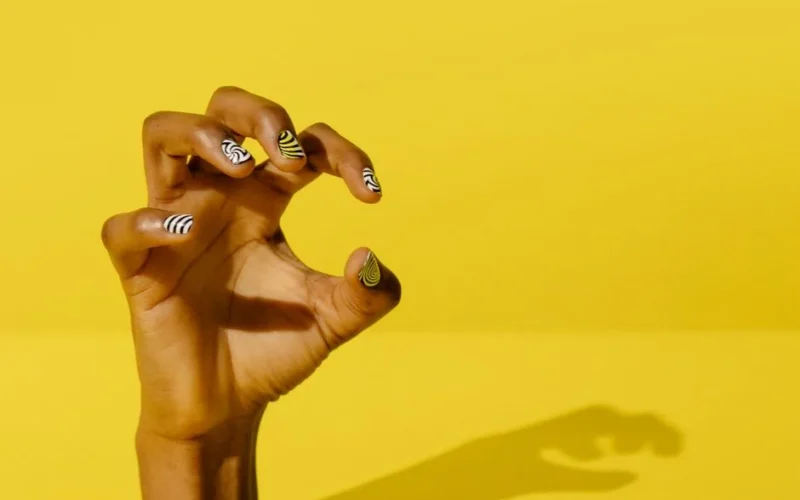 Close-up of a hand with artistic nail polish against a yellow background.