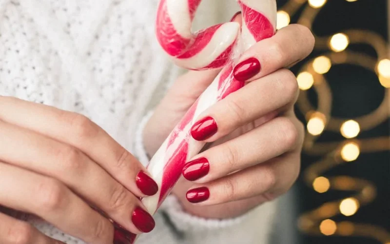 Close-up of hands with red nails holding a candy cane, perfect for Christmas-themed visuals.
