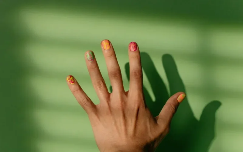 Close-up of a hand with intricate nail art casting shadows on a green surface.