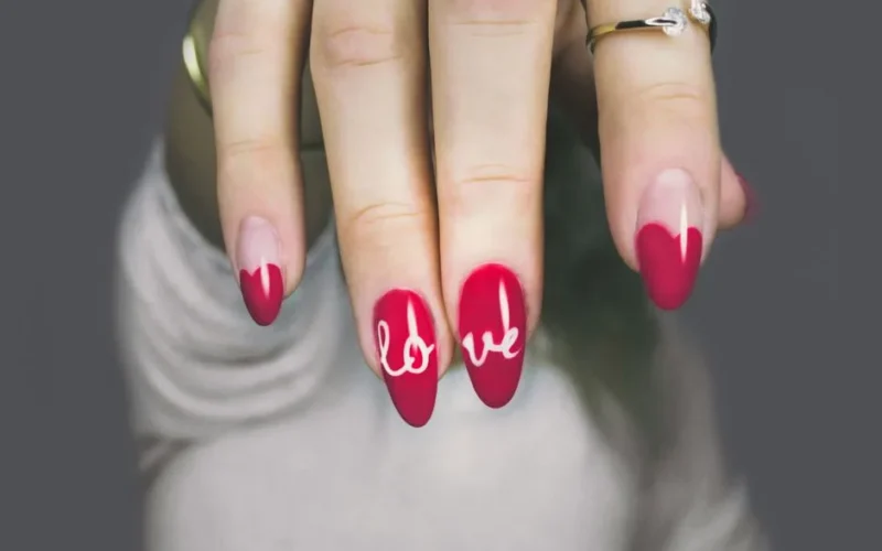 Vibrant red nails with 'love' art on a woman's hand, showcasing elegant style and design.