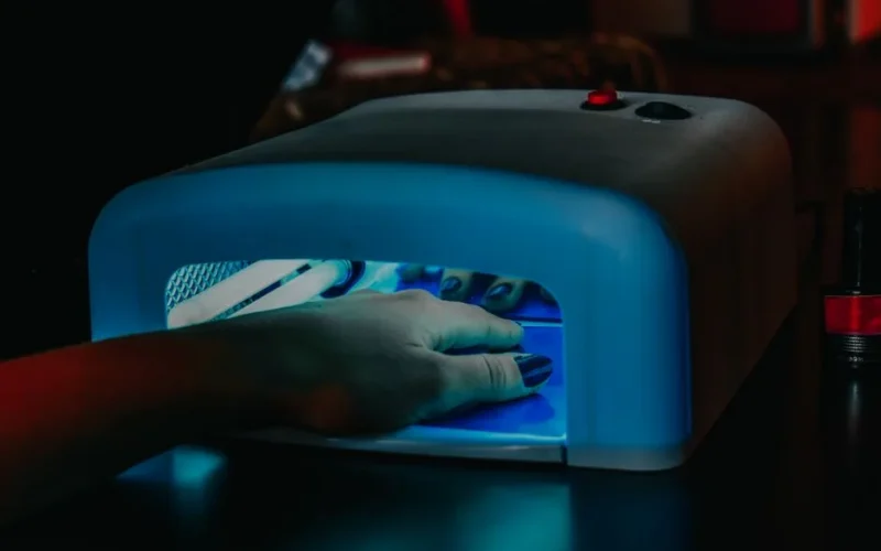 A hand with manicured nails being cured under a blue LED lamp for gel polish.