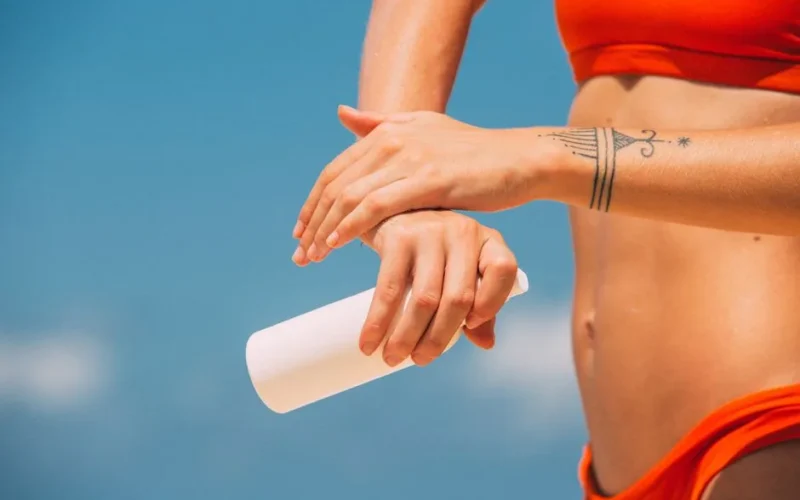 Close-up of a woman applying sunscreen on the beach with a blue sky background.