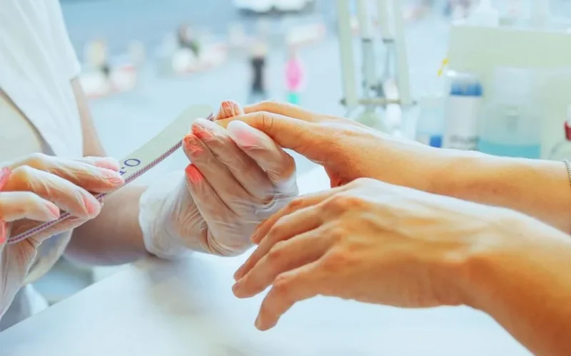 Close-up of a manicurist performing a nail file treatment on a customer's hand in a salon.