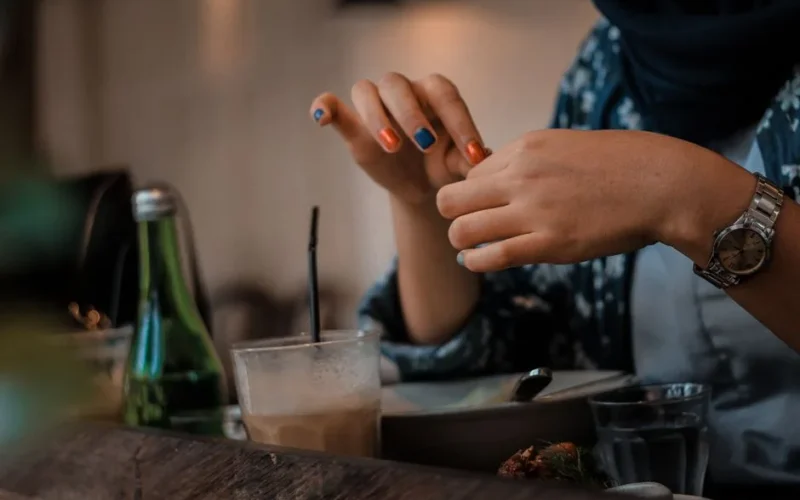 A woman's hands with colorful nails enjoying a drink at an indoor table.