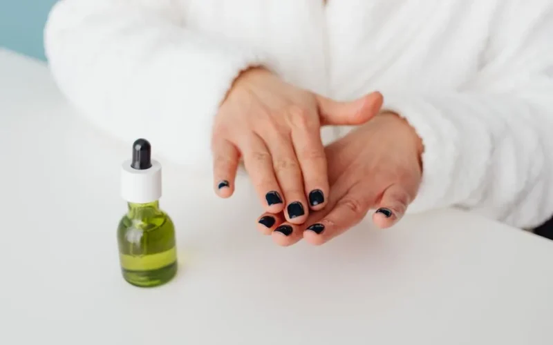 Close-up of hands applying essential oil with green bottle, focusing on nail care.